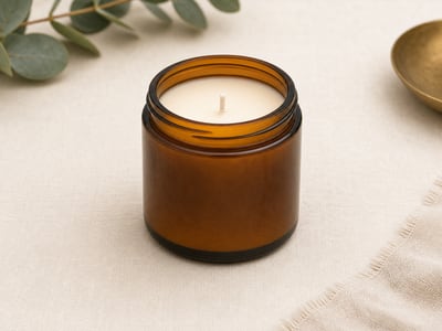 Amber glass jar candle with cream wax on an ivory surface